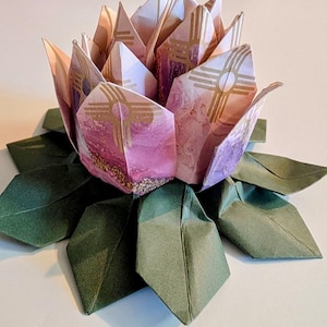 May include: An origami lotus flower in pink and gold tones, with green paper leaves. The petals are crafted from patterned paper, demonstrating detailed folding techniques. The flower is a decorative piece, showcasing the art of paper folding.