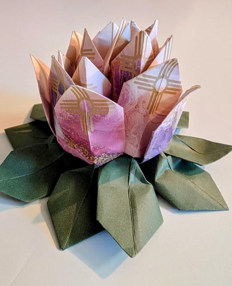 May include: An origami lotus flower in pink and gold tones, with green paper leaves. The petals are crafted from patterned paper, demonstrating detailed folding techniques. The flower is a decorative piece, showcasing the art of paper folding.