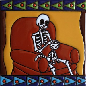 May include: A ceramic tile with a colorful design featuring a skeleton sitting in a red armchair with a small skeleton cat on its lap. The tile has a yellow background and a blue and green border.