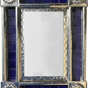 May include: A rectangular mirror with a silver frame, adorned with blue square tiles and decorative silver accents. The corners feature silver floral designs. The mirror's frame has a textured, rope-like pattern.
