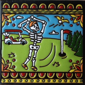 May include: A colorful ceramic tile with a skeleton golfer swinging a golf club. The tile has a green background with a blue sky and white clouds. There is a golf cart in the background and a red flag on a golf hole.
