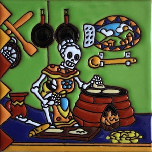 May include: A colorful ceramic tile depicting a skeleton wearing a red, yellow, and blue dress, making tortillas on a clay oven. The tile has a green background with a blue and white fish design and other kitchen items.