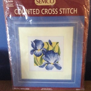 May include: A Semco counted cross stitch kit in plastic packaging featuring a blue iris flower design on a light yellow background. The package includes the text Anchor, Semco, Counted Cross Stitch, Kit No. 6016.3000, and Iris printed on the front.