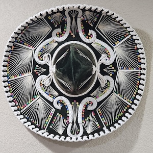 May include: A black sombrero with intricate white embroidery and colorful bead accents. The hat features a rounded crown and a wide, flat brim, showcasing a traditional Mexican design.