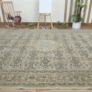 May include: Large, rectangular area rug with an intricate, traditional design. The rug features a central medallion and border in shades of beige, blue, and brown. The rug is placed on a wooden floor.