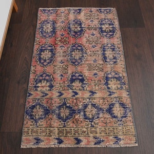 Puede incluir: Una alfombra vintage con un patrón rosa, azul y beige. La alfombra tiene un aspecto desgastado y está hecha de lana. Mide aproximadamente 60 cm por 90 cm.