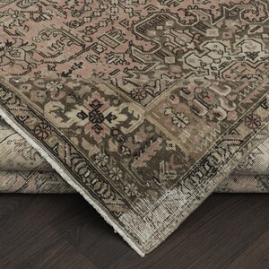May include: An antique area rug with a detailed, faded floral pattern in shades of pink, brown, and beige. The rug's corner is folded back, revealing the underside and the intricate design of the border.