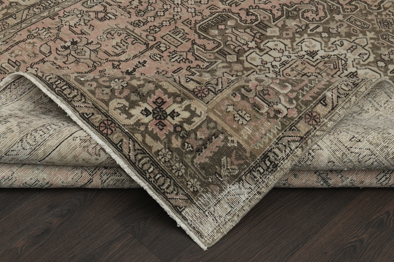 May include: An antique area rug with a detailed, faded floral pattern in shades of pink, brown, and beige. The rug's corner is folded back, revealing the underside and the intricate design of the border.