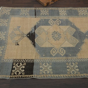 May include: A vintage rug with a beige background and a blue and black geometric pattern. The rug has a fringed edge.
