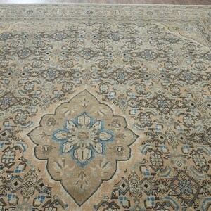 May include: A large, rectangular area rug with an intricate, traditional design. The rug features a central medallion with a floral motif in shades of blue and beige, surrounded by a repeating pattern in similar tones. The overall color palette is muted, with a vintage aesthetic.