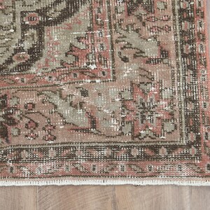Puede incluir: Una alfombra vintage con un patr&oacute;n floral descolorido en rosa y marr&oacute;n. La alfombra tiene un aspecto desgastado y un borde con flecos.