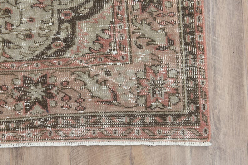 Puede incluir: Una alfombra vintage con un patr&oacute;n floral descolorido en rosa y marr&oacute;n. La alfombra tiene un aspecto desgastado y un borde con flecos.