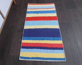 May include: A colorful striped rug with blue, yellow, red, and white stripes. The rug is made of a woven fabric and has a fringed edge.