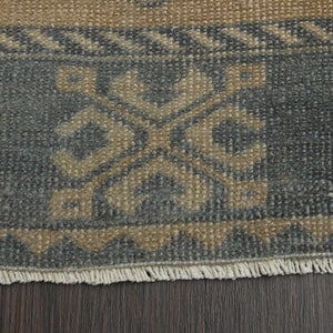 May include: Close-up of a rug with a blue and beige geometric pattern. The rug has a fringed border.