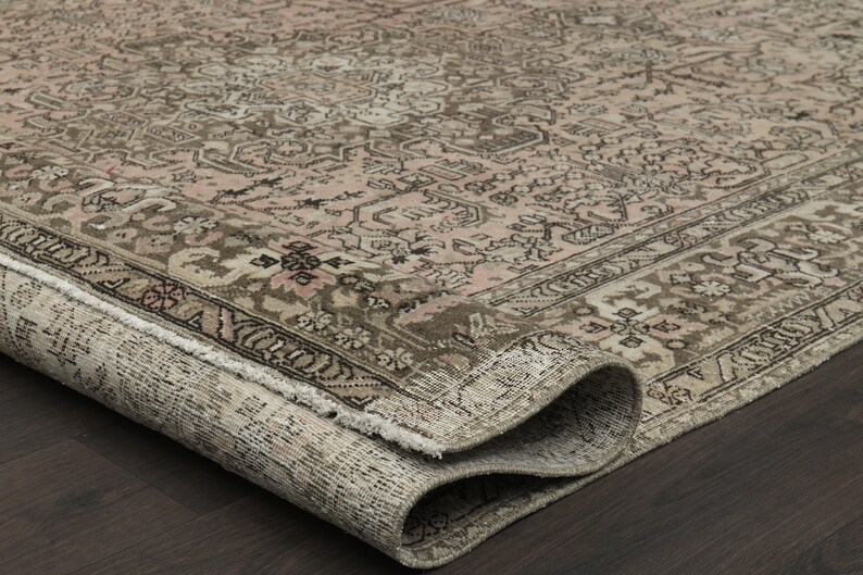 May include: A rolled-up, vintage rug with a faded, distressed look. It has a complex floral pattern in beige, brown, and pink. The edges are frayed, adding to its antique charm. The rug is on a dark wood surface.