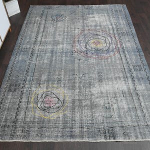 May include: A vintage-style rug with a gray background and colorful embroidered floral designs. The rug has a distressed look and a faded appearance.