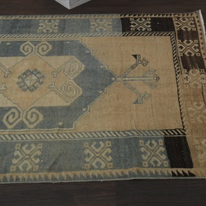 May include: A vintage rug with a beige background and a blue and black geometric pattern. The rug has a fringed edge.