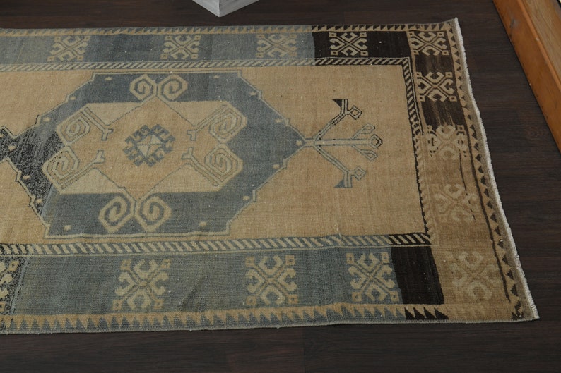 May include: A vintage rug with a beige background and a blue and black geometric pattern. The rug has a fringed edge.