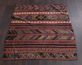 May include: A vintage Turkish kilim rug with a geometric pattern in shades of red, blue, black, and white. The rug has a fringed edge and is woven with wool.