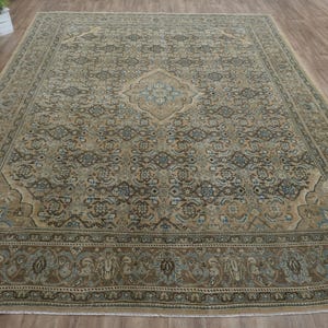 May include: Large rectangular area rug with an intricate, traditional pattern. The rug features a central medallion and border in shades of brown, beige, and blue. The rug is placed on a wooden floor.