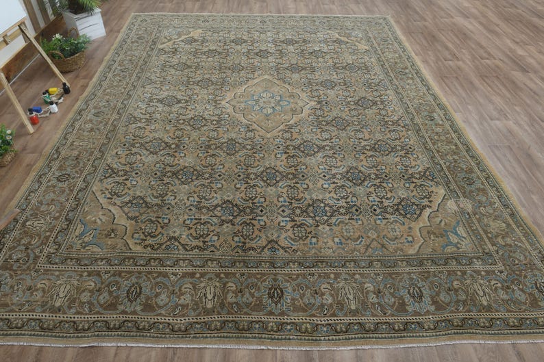 May include: Large rectangular area rug with an intricate, traditional pattern. The rug features a central medallion and border in shades of brown, beige, and blue. The rug is placed on a wooden floor.