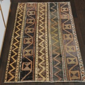 Op de afbeelding: Een vintage tapijt met een geometrisch patroon in tinten bruin, beige en groen. Het tapijt heeft een versleten en verbleekte uitstraling, waardoor het een rustieke en antieke uitstraling heeft.