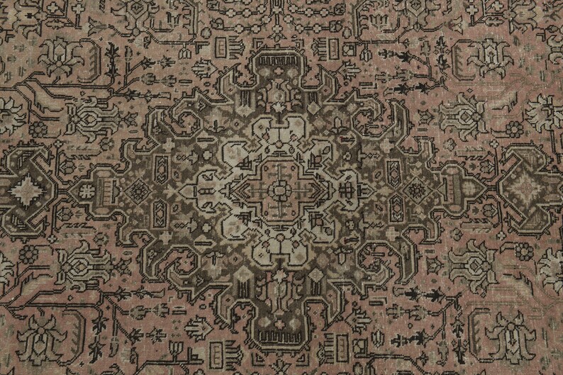 May include: Close-up of a vintage rug with an elaborate, symmetrical design. The rug's colour palette includes muted tones of dusty rose, brown, and cream. The pattern incorporates floral and geometric motifs.