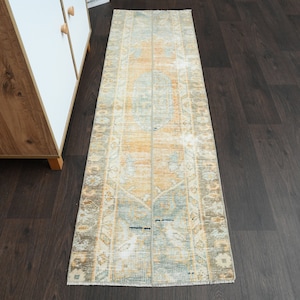 May include: A vintage runner rug with a faded, distressed look. The rug has a light blue, beige, and orange color scheme with a floral pattern.
