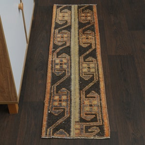 May include: A long, narrow rug with a geometric pattern in shades of orange, brown, and beige. The rug has a fringe on both ends.