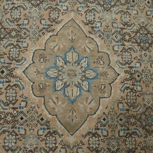 May include: An antique-style rug with a central medallion design. The rug features a beige background with intricate patterns in shades of brown, blue, and cream. The central medallion is a focal point, with a floral design in blue and beige.