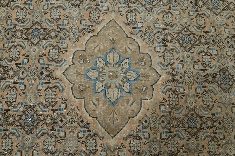 May include: An antique-style rug with a central medallion design. The rug features a beige background with intricate patterns in shades of brown, blue, and cream. The central medallion is a focal point, with a floral design in blue and beige.