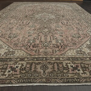May include: A large, rectangular rug with a detailed, traditional design. The rug has a central field of muted pink, framed by brown and beige borders. The pattern incorporates floral and geometric elements.