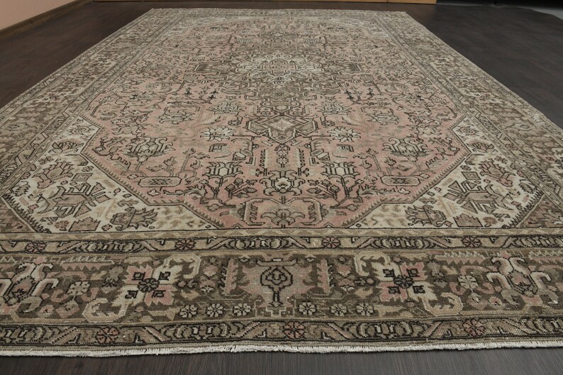 May include: A large, rectangular rug with a detailed, traditional design. The rug has a central field of muted pink, framed by brown and beige borders. The pattern incorporates floral and geometric elements.