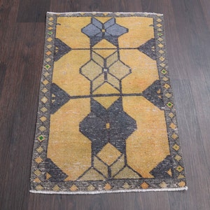 Puede incluir: Una alfombra de color amarillo y negro con un patrón geométrico y un borde verde y blanco. La alfombra está sobre un suelo de madera oscura.