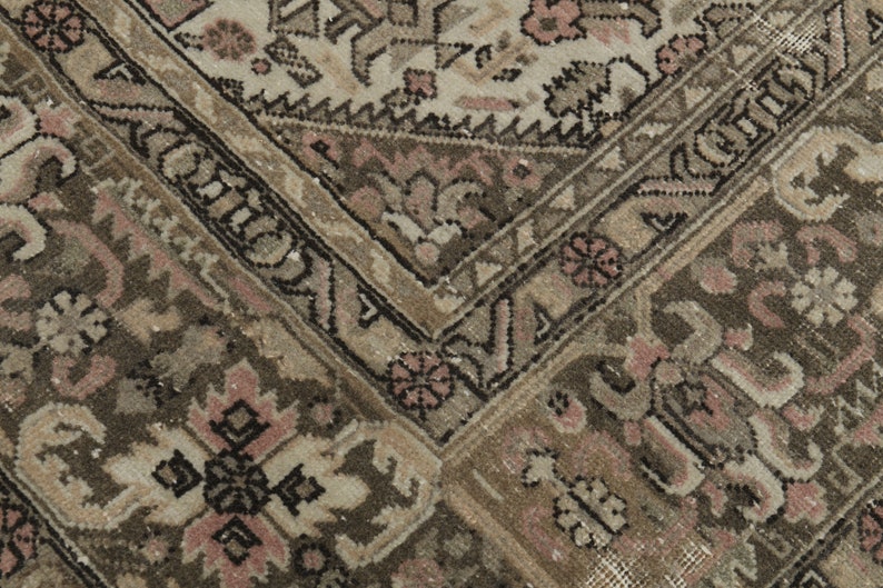May include: Close-up of a vintage rug with a detailed pattern. The rug features a combination of beige, brown, and pink tones. The design includes floral and geometric elements, creating a textured and aged appearance.