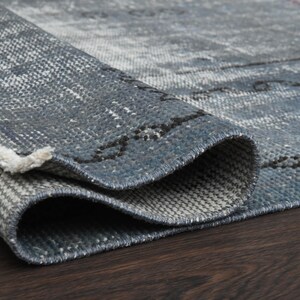 May include: Close-up of a blue and gray rug with a woven texture. The rug is folded in half, showing the underside of the rug.
