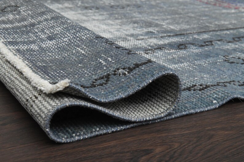 May include: Close-up of a blue and gray rug with a woven texture. The rug is folded in half, showing the underside of the rug.