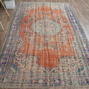 May include: An orange and blue distressed area rug with a central medallion design. The rug features a faded, vintage look with floral and geometric patterns. The rug is rectangular and suitable for a living room or bedroom.