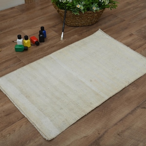 May include: A white rectangular rug with a subtle woven texture. The rug is lying on a wooden floor.
