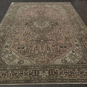 May include: A large, rectangular rug with an intricate, traditional design. The rug features a central medallion in shades of pink and beige, surrounded by a detailed border in brown and cream. The overall pattern is ornate and symmetrical.