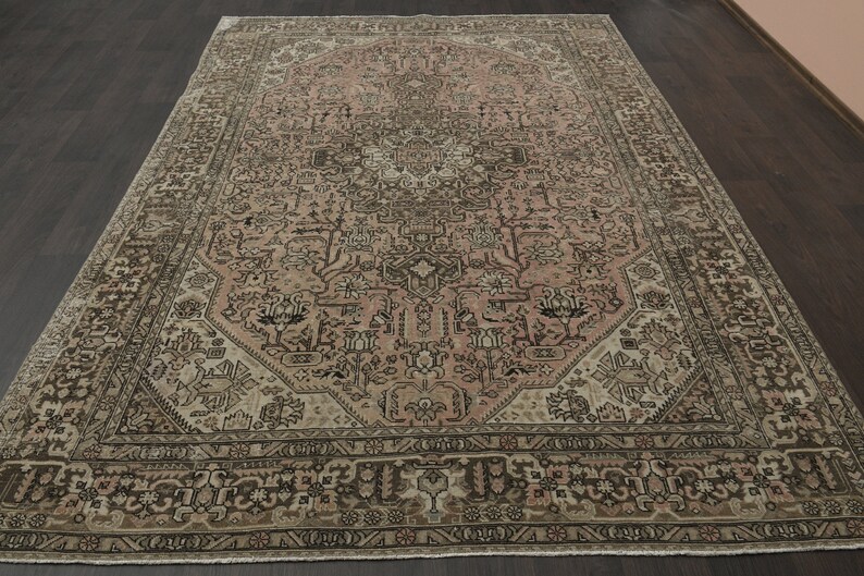 May include: A large, rectangular rug with an intricate, traditional design. The rug features a central medallion in shades of pink and beige, surrounded by a detailed border in brown and cream. The overall pattern is ornate and symmetrical.