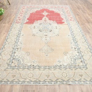 May include: A vintage rug with a light beige background and a red center. The rug has a floral pattern with a border of blue and gray.