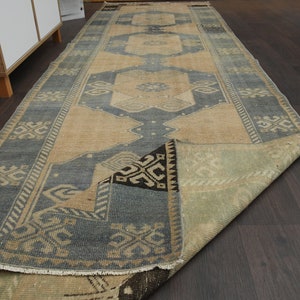 May include: A vintage runner rug with a blue and beige geometric pattern. The rug is folded in half and has a fringe border.