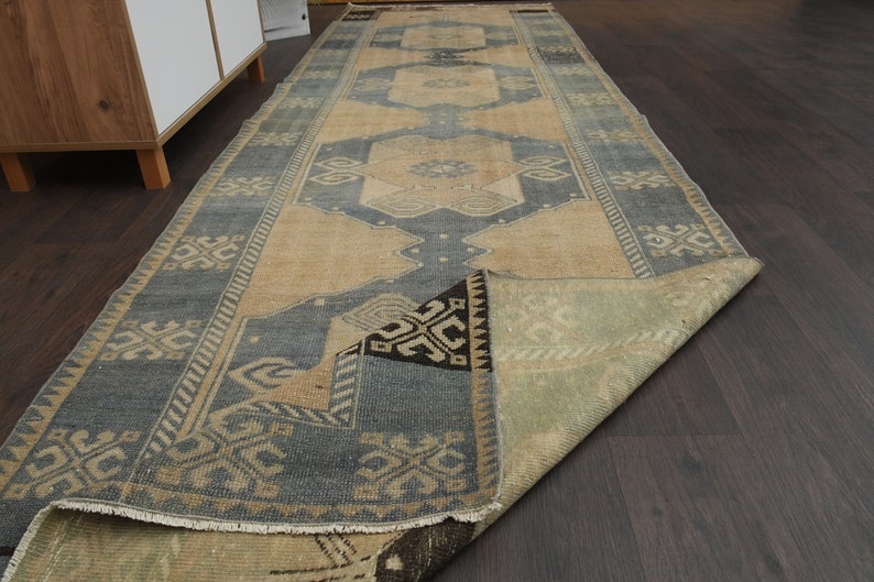May include: A vintage runner rug with a blue and beige geometric pattern. The rug is folded in half and has a fringe border.