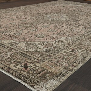 May include: A large, rectangular rug with a detailed floral design. The rug has a central pale pink field, framed by a brown and beige border. The overall appearance is vintage, with a distressed finish.
