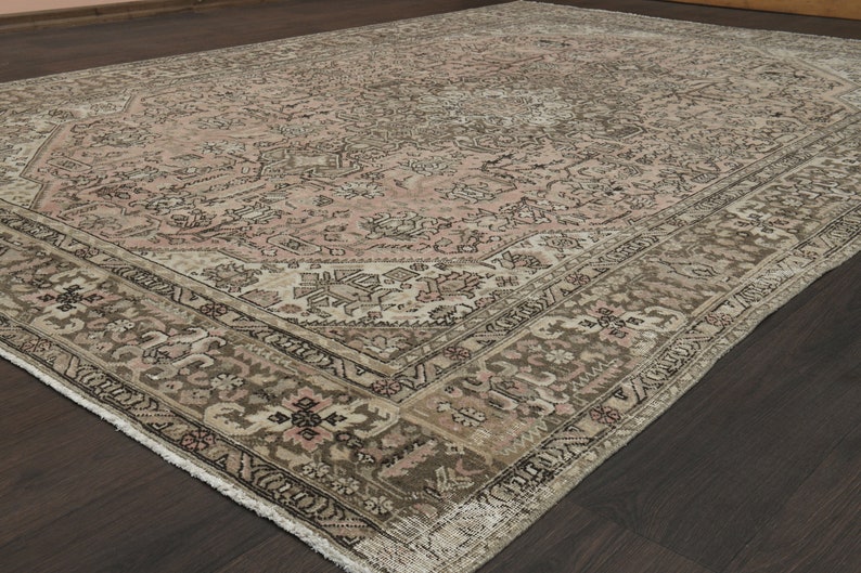 May include: A large, rectangular rug with a detailed floral design. The rug has a central pale pink field, framed by a brown and beige border. The overall appearance is vintage, with a distressed finish.