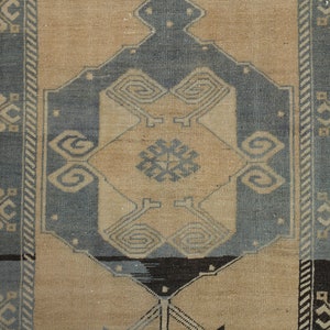 May include: A vintage rug with a beige background and a blue and black geometric pattern. The rug has a border with a repeating pattern of stylised flowers.