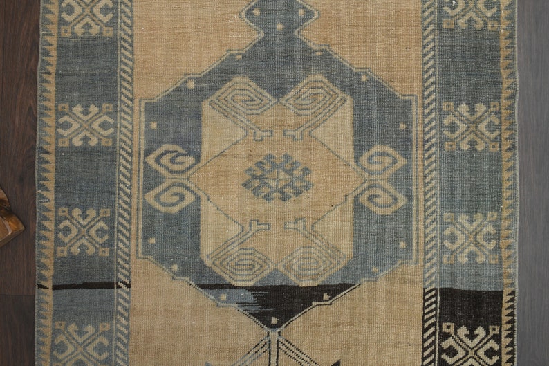 May include: A vintage rug with a beige background and a blue and black geometric pattern. The rug has a border with a repeating pattern of stylised flowers.