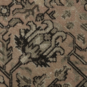 May include: Close-up of a section of a vintage rug with a detailed floral pattern. The rug features a colour palette of muted pink, beige, and black, with intricate designs and a textured surface. The rug's design is symmetrical.
