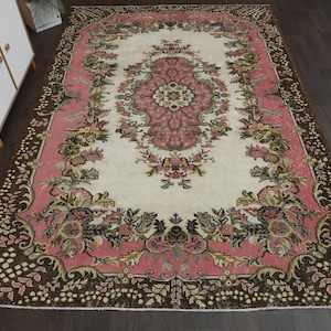 May include: A vintage rug with a floral pattern in shades of pink, brown, and cream. The rug has a central medallion with a floral design and a border with a repeating floral motif.
